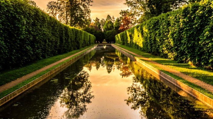 The long still canal between towering hedges at Antrim Castle Gardens at sunset
