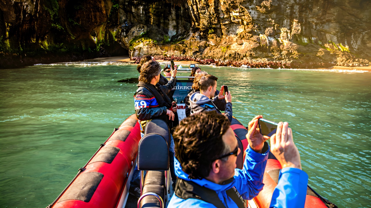 Passengers lean out to photograph a sheltered sea cave, its water a clear jade green