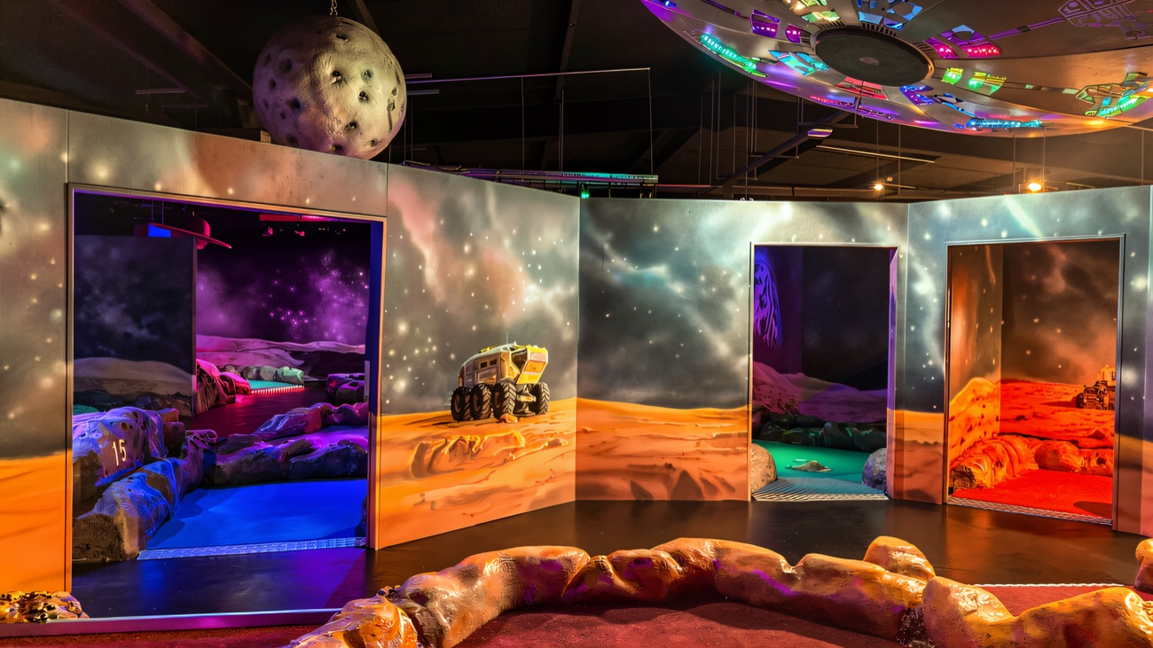 The space course glows with a Mars-rover mural, hanging planet and neon-lit UFO ceiling