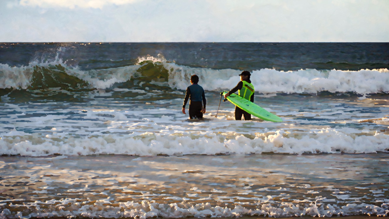 Instructor and surfer wade out to meet a clean grey-day set