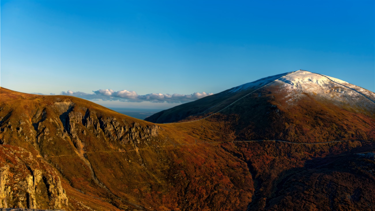 Rocky crags on the shoulder of a Mourne hill, with a snow-dusted summit under a clear blue sky.