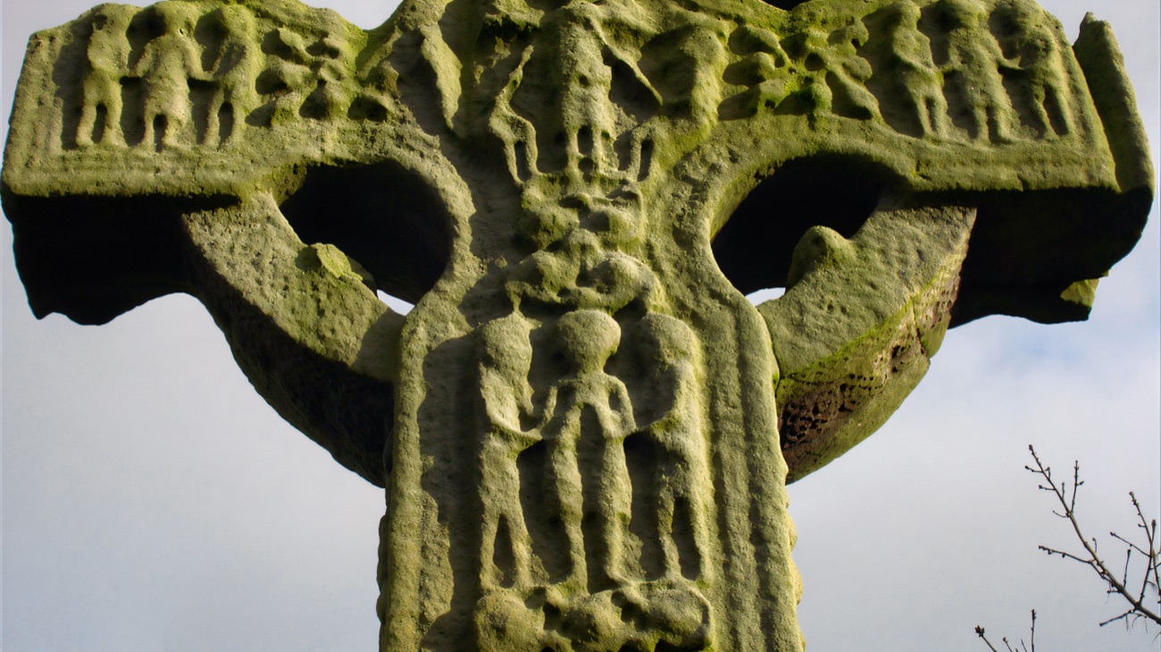 A close look at the weathered biblical carvings ringed with moss near the head of the cross.