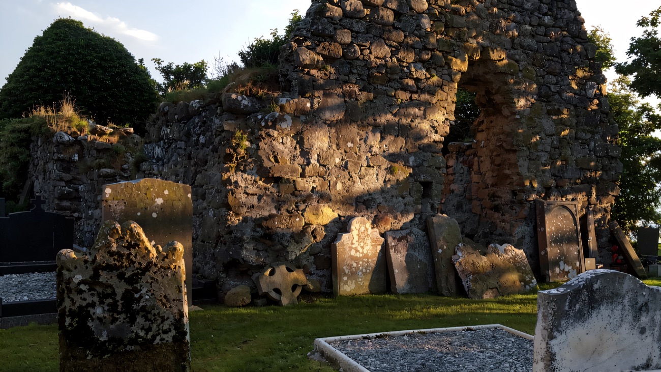 The ruined walls and old graveyard of the early monastic site that grew up beside the cross.