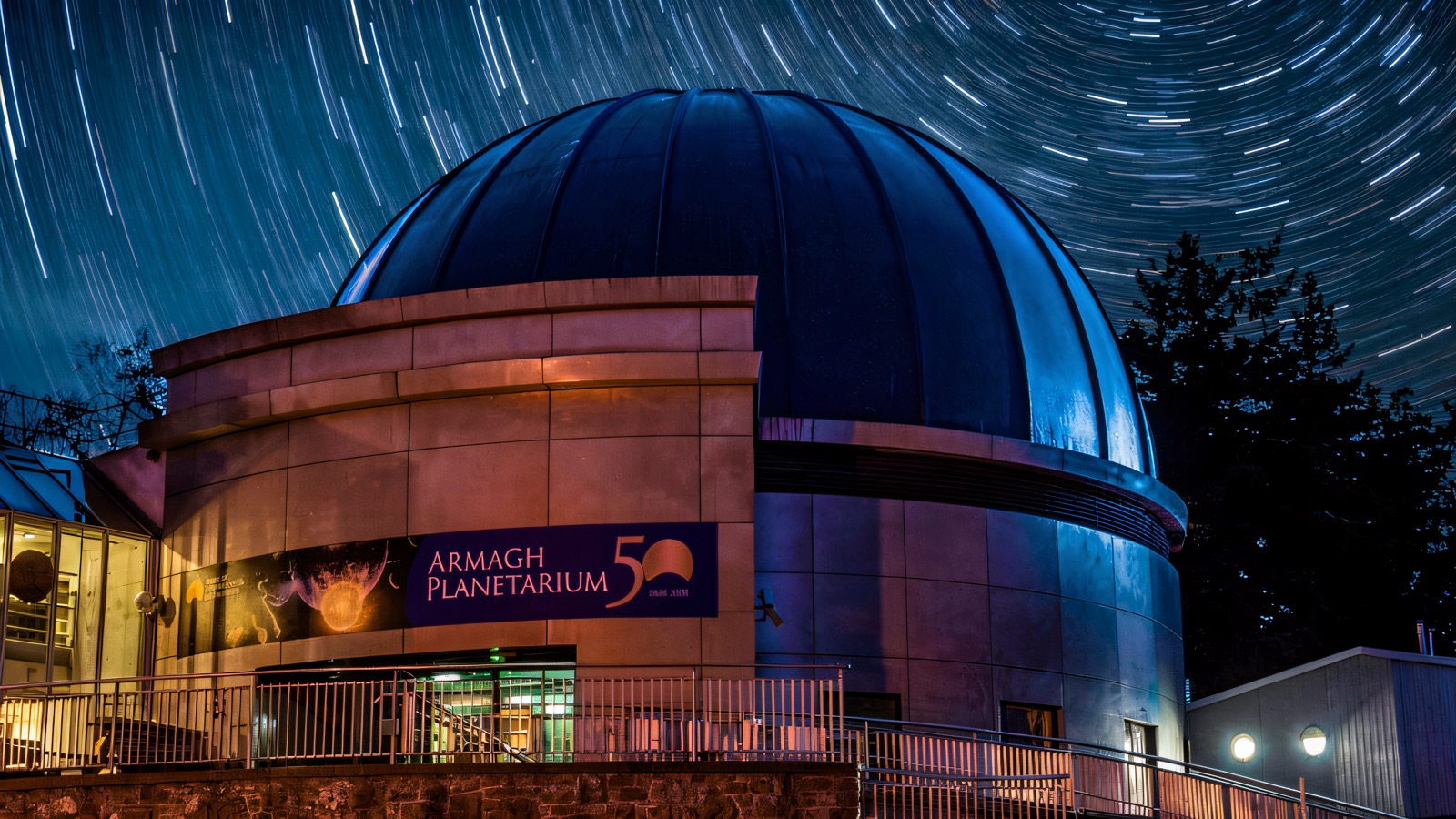 The domed planetarium building at night under a sky of star-trails