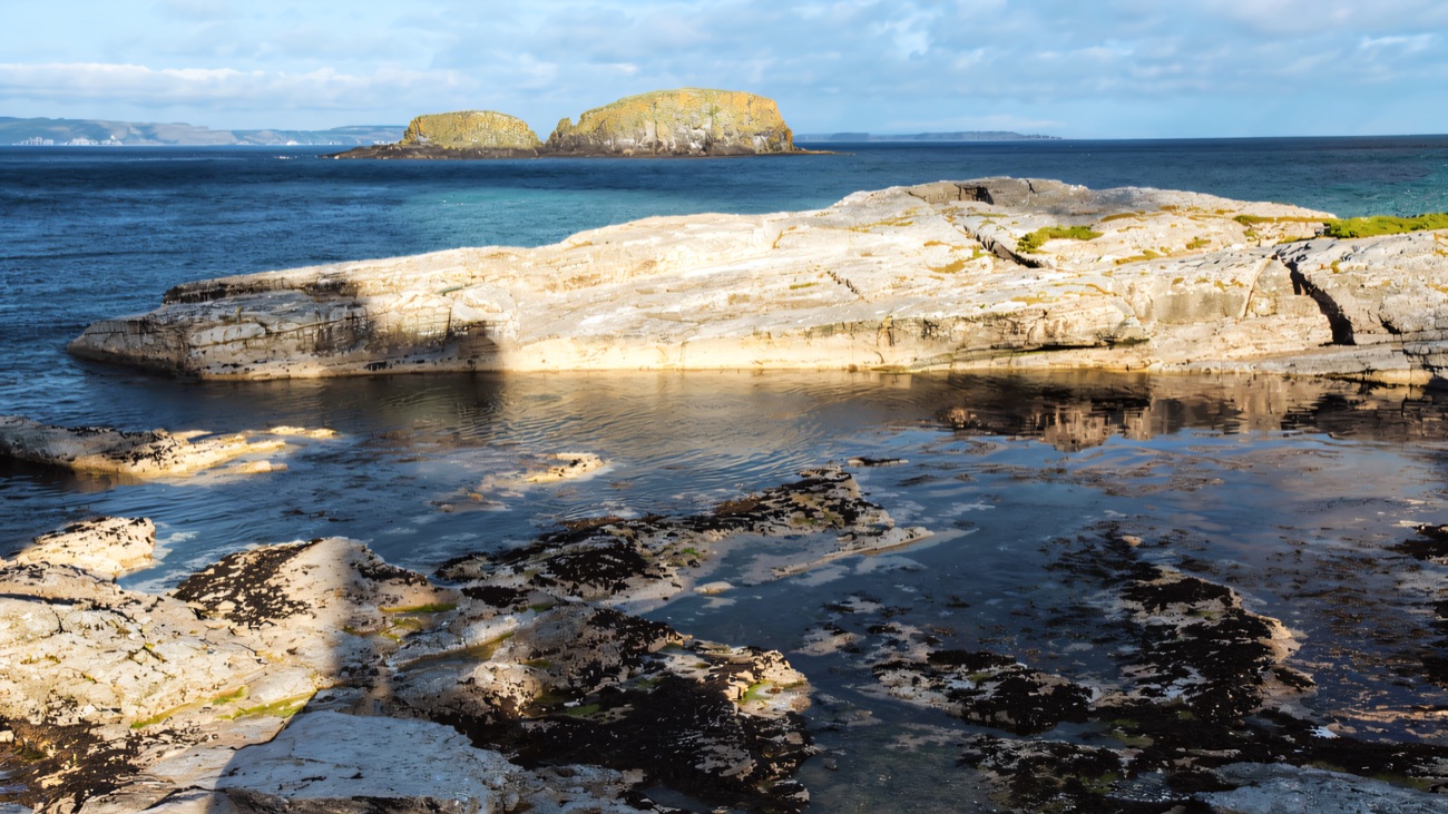 Rock pools on the limestone foreshore at Ballintoy with sea stacks rising offshore