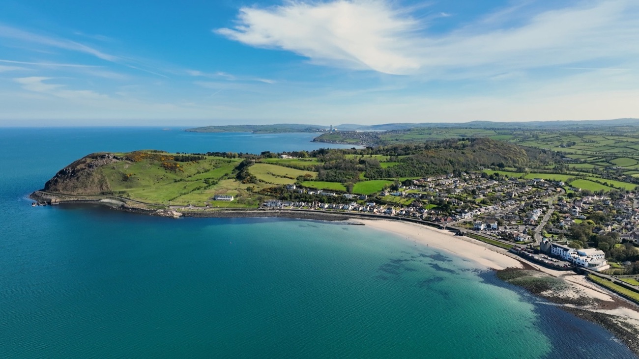 Aerial view of Ballygally bay, the crescent of sand, the village and the green headland on the Antrim coast