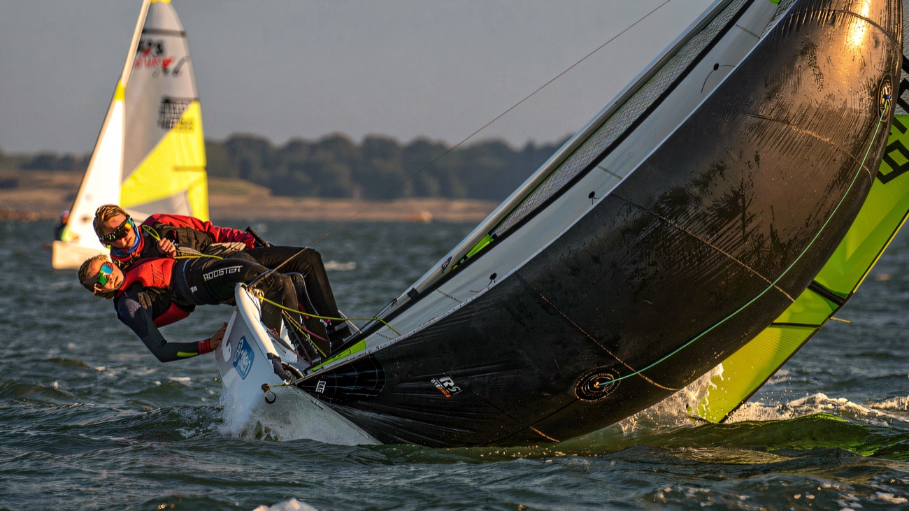 A skiff crew flat out on the trapeze, sail full and driving