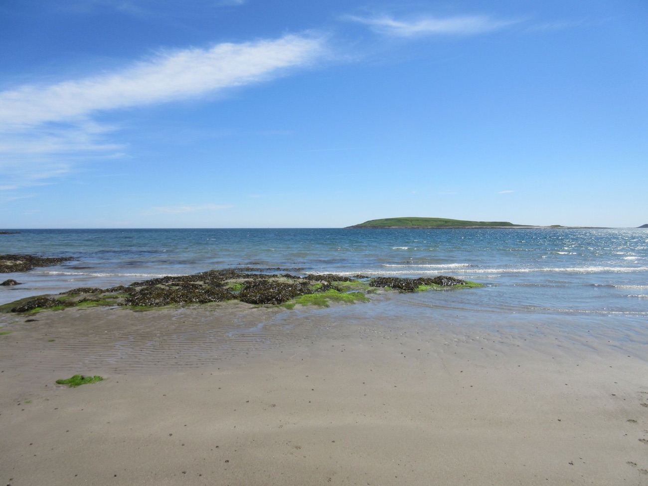 Looking out from the sands of Ballyhornan across calm blue sea to green Guns Island on the horizon under a bright sky