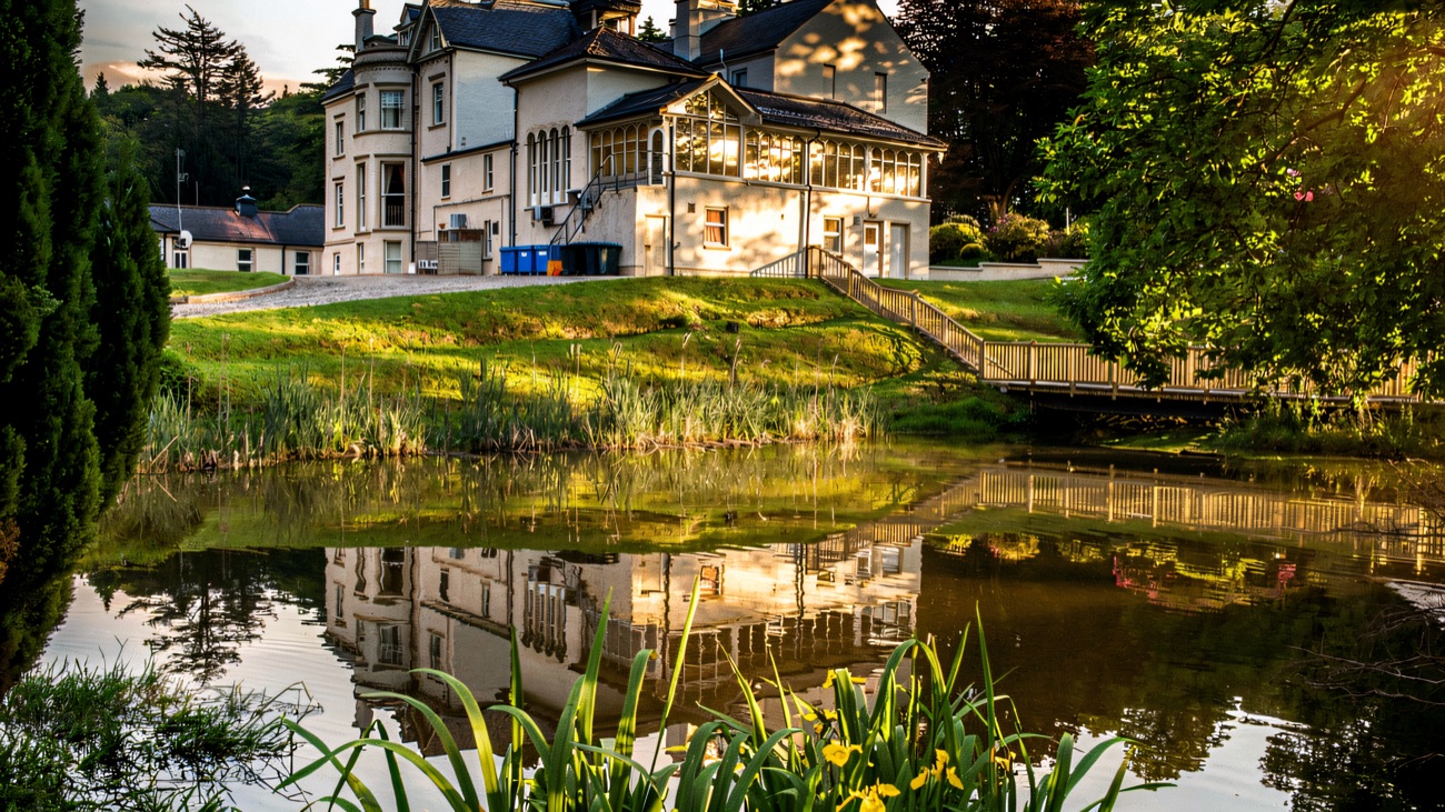 The house reflected in one of the grounds' ponds, with yellow flag irises in the foreground and a wooden footbridge