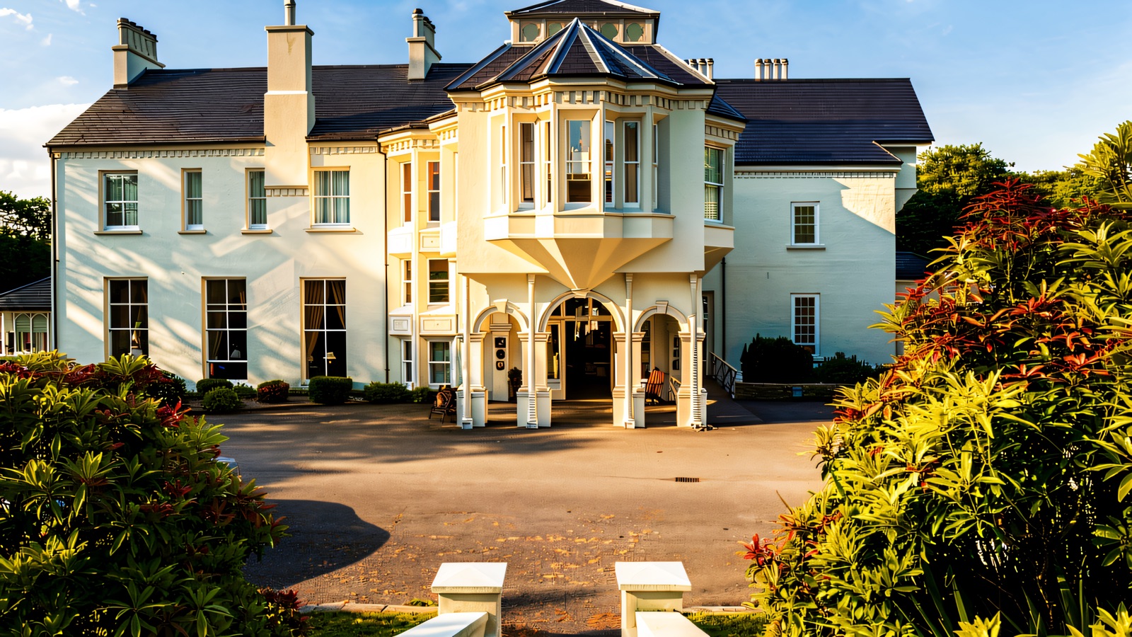 The cream-rendered Georgian front of Beech Hill Country House with its arched porch and bay tower, framed by red and green shrubs