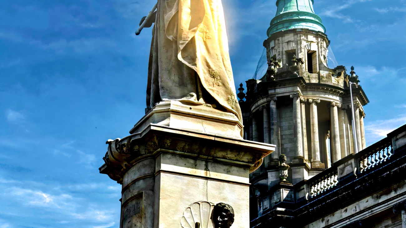 The white marble Queen Victoria statue in the grounds of Belfast City Hall with a green copper dome behind