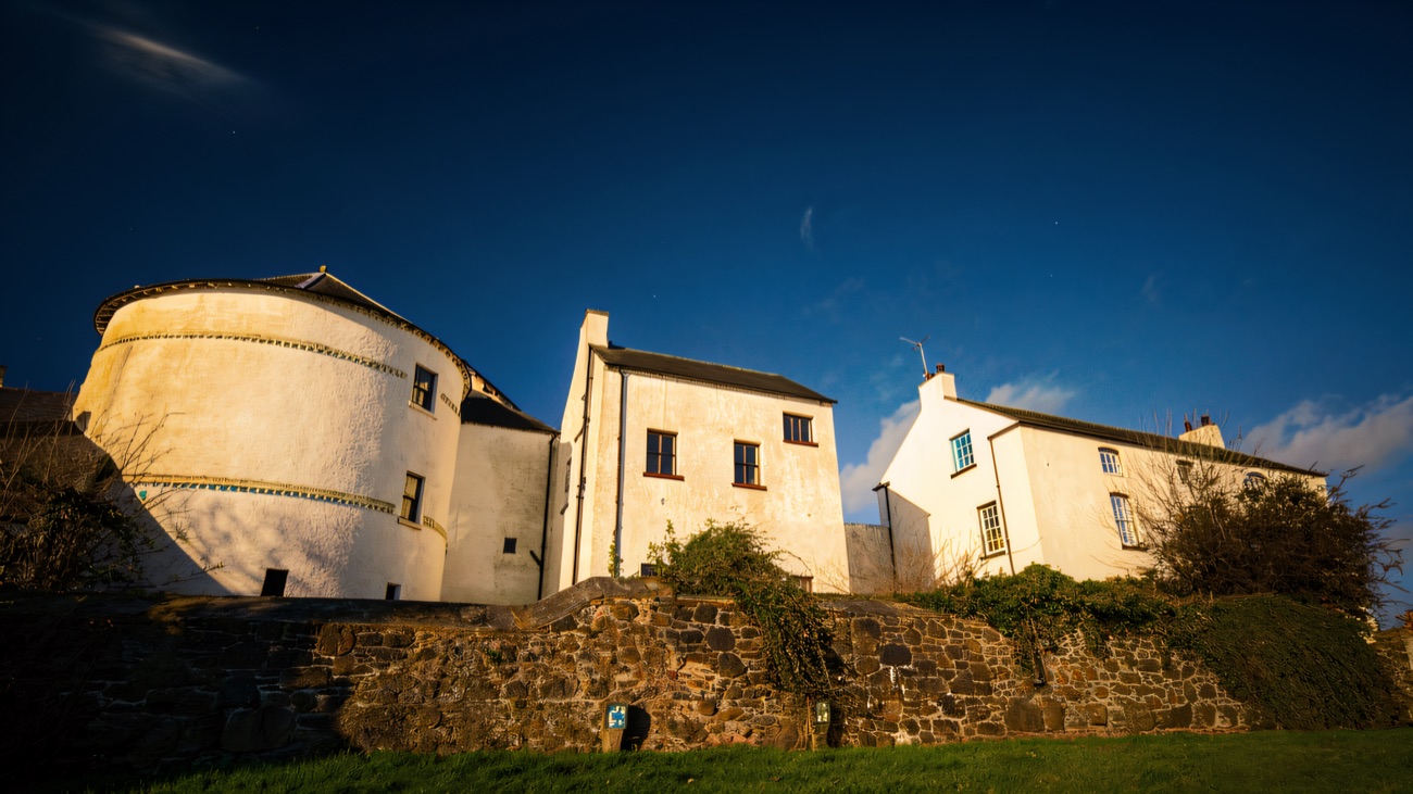 The round flanker tower and fortified house at Bellaghy Bawn seen over the old stone wall against a blue sky