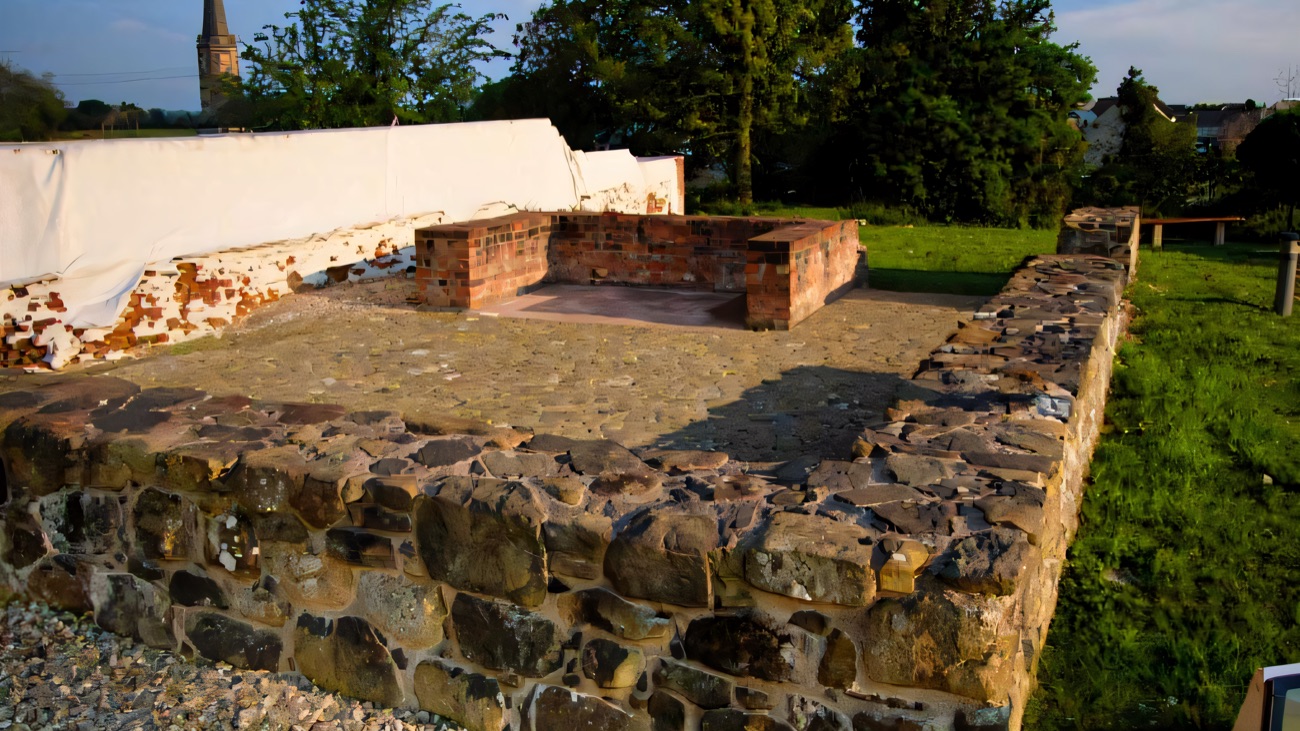 Excavated stone wall footings of the Plantation bawn at Bellaghy, with the village church spire behind