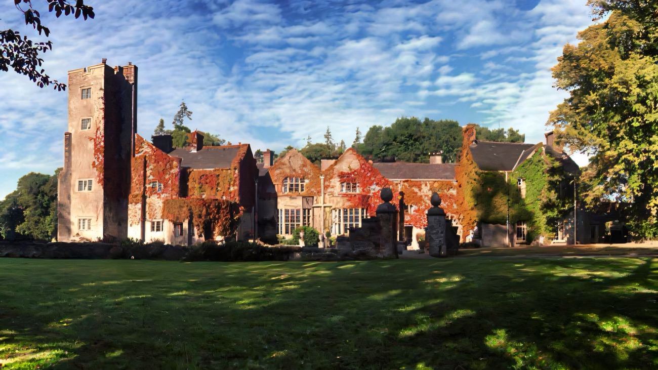 Belle Isle Castle under a blue sky, its walls turning red with autumn ivy, statues on the lawn