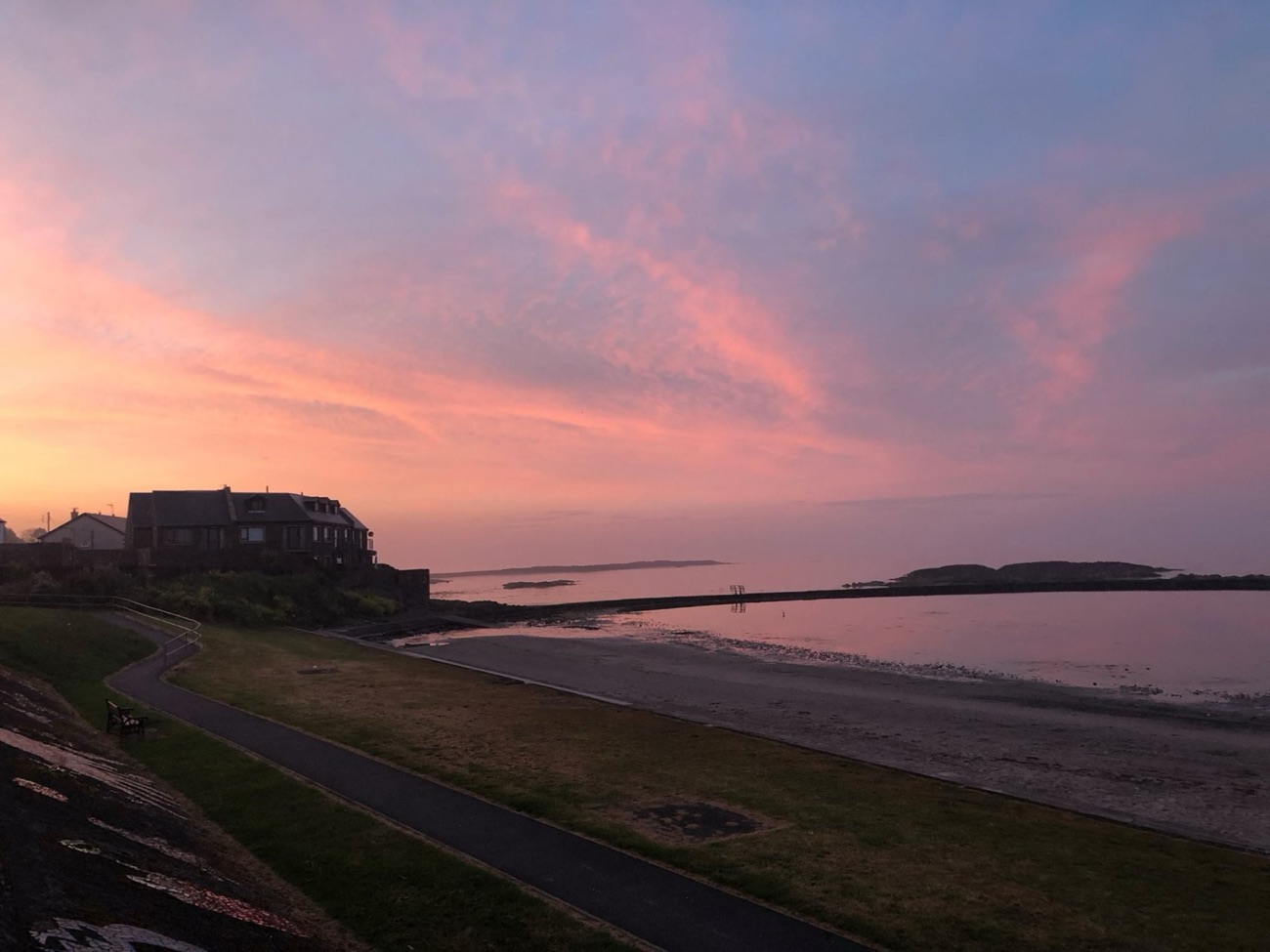 Evening light over the seawater lagoon and sandy beach at Millisle with the promenade path in the foreground