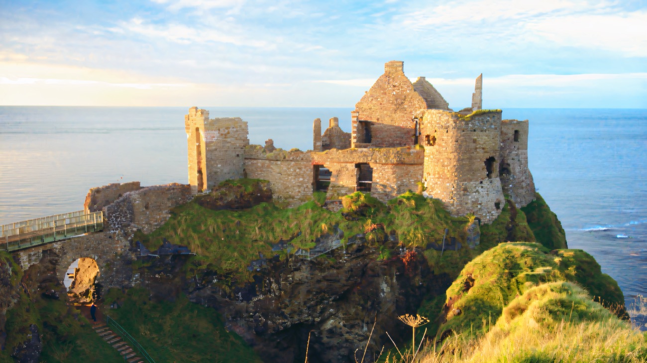 The ruins of Dunluce Castle standing on their own sea stack above the Atlantic in golden light