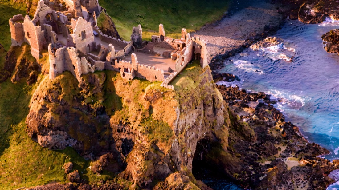 Aerial view of the clifftop ruins of Dunluce Castle above turquoise water