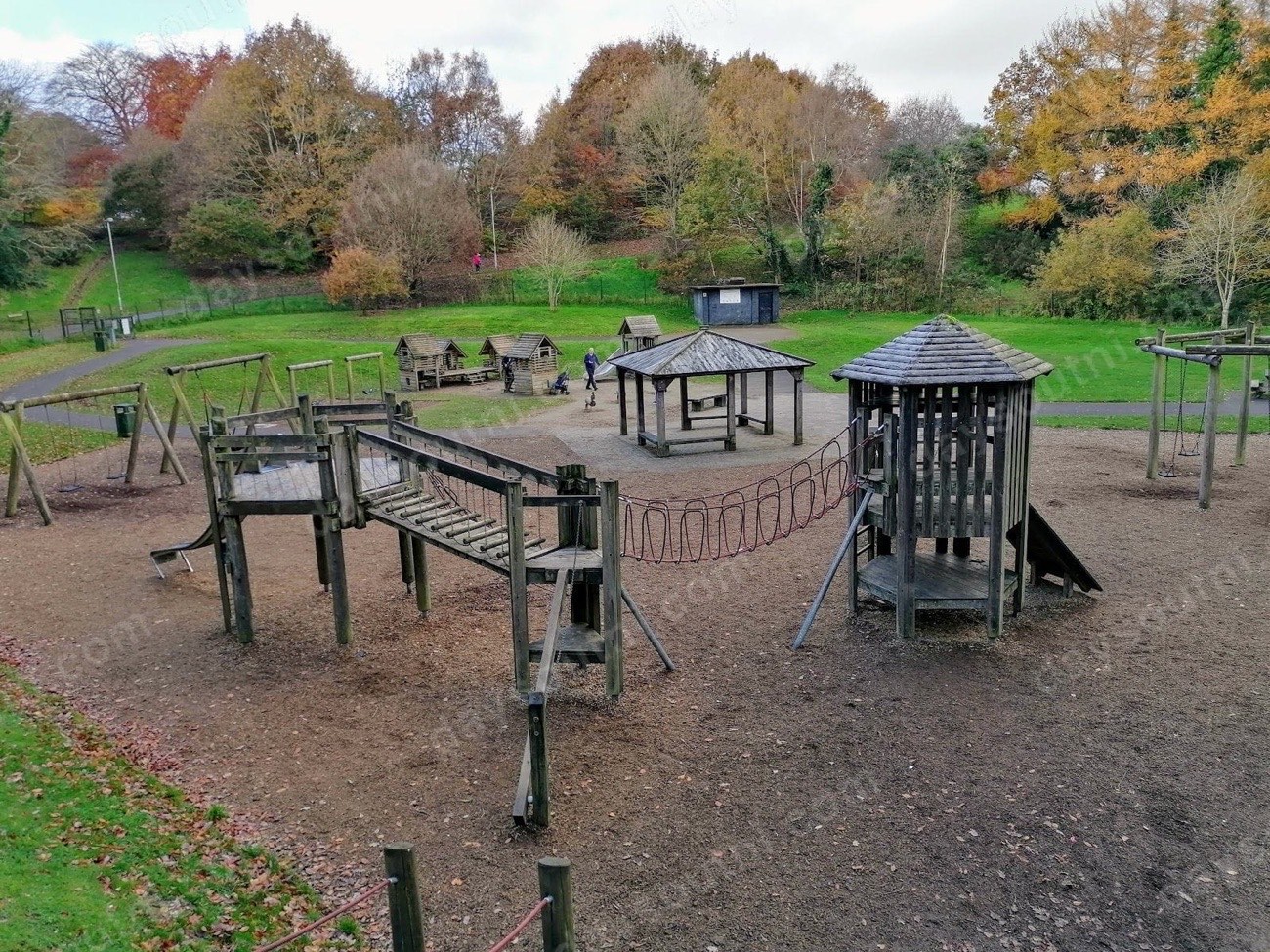 Wooden climbing frames and towers of St Columb's Park playground surrounded by autumn trees in Derry