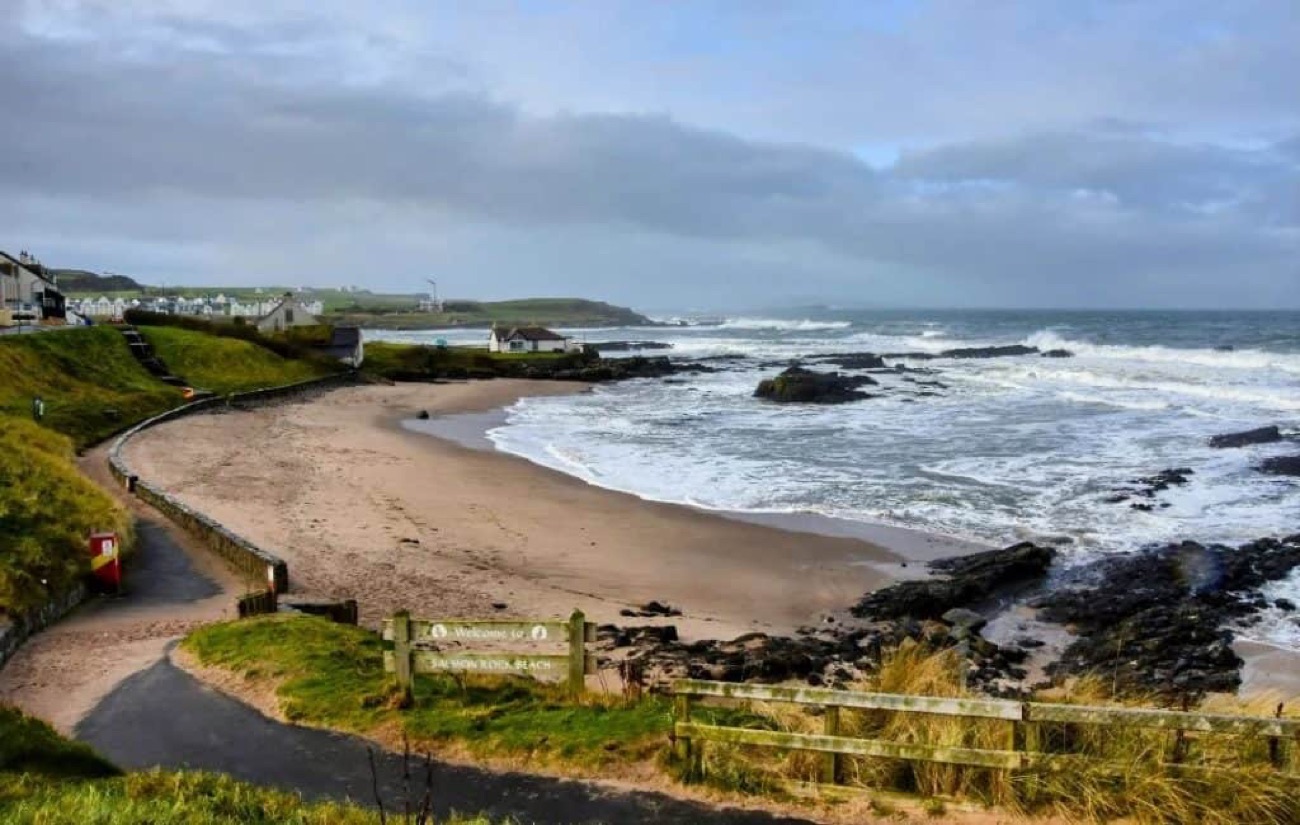 Salmon Rock Beach at Portballintrae with its welcome sign, sand and rocky headland