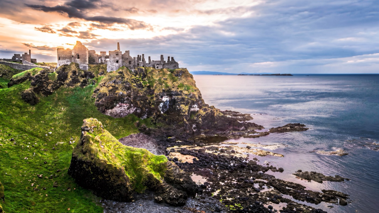 The ruins of Dunluce Castle perched on a rocky headland above the sea at dusk