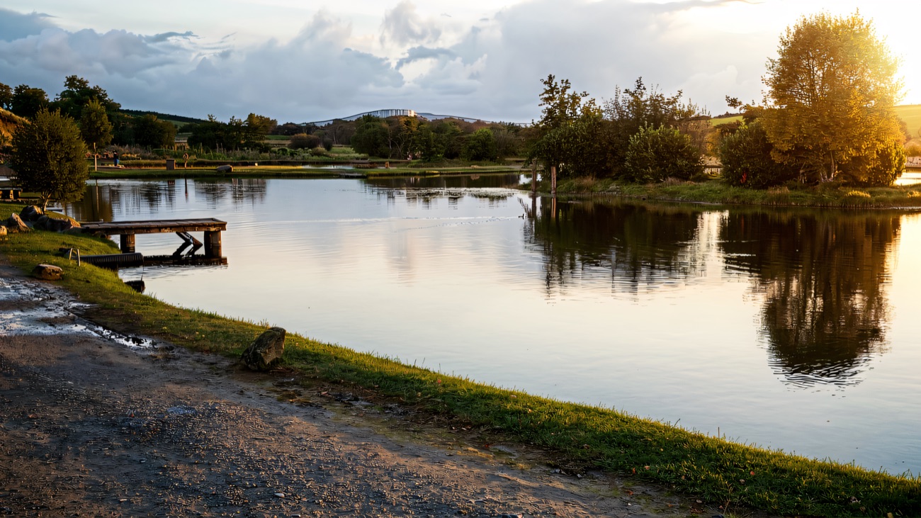 The still fishery lake at dusk, jetties and low hills mirrored in the calm water