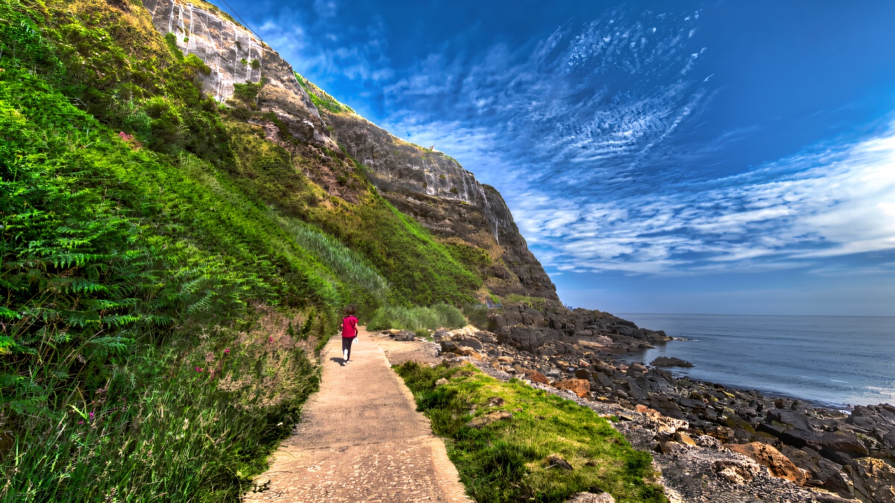 A walker on the Blackhead path beneath the towering cliff