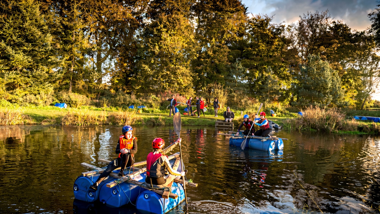Home-made barrel rafts being paddled across the lake on a sunny afternoon