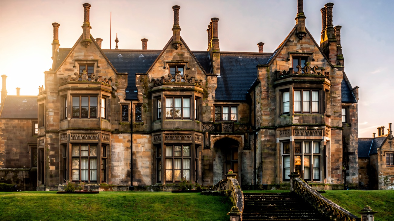 The ornate Elizabethan-style facade of Brownlow House with twin bay windows and a stone staircase up to the lawn