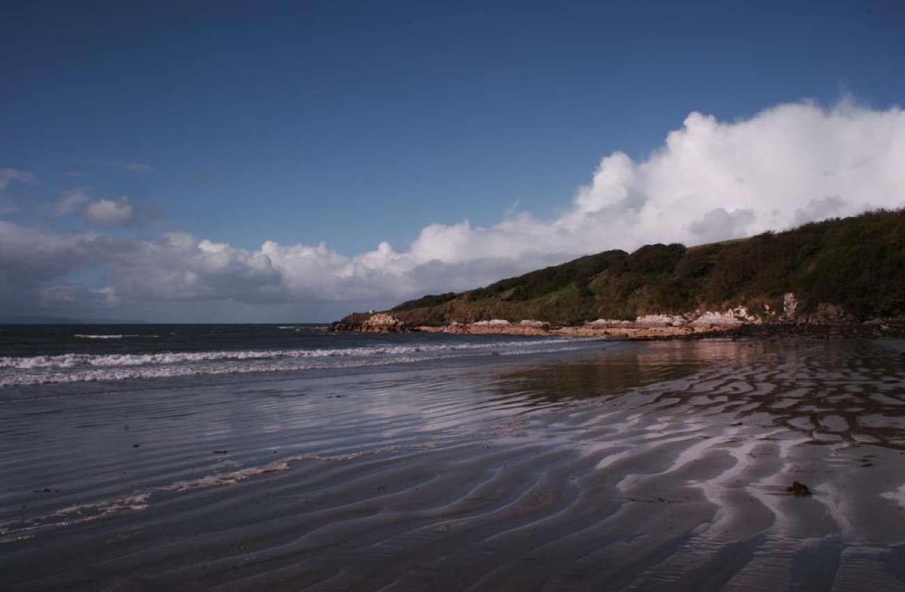 Rippled wet sand at low tide with a rocky point and green cliffs along the Islandmagee coast