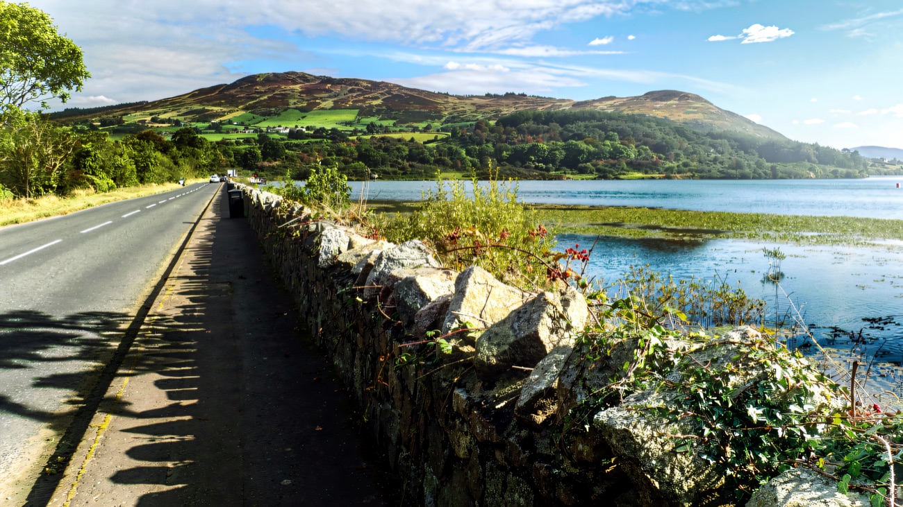 The lakeside road and old stone wall, with the mountains rising beyond the water.