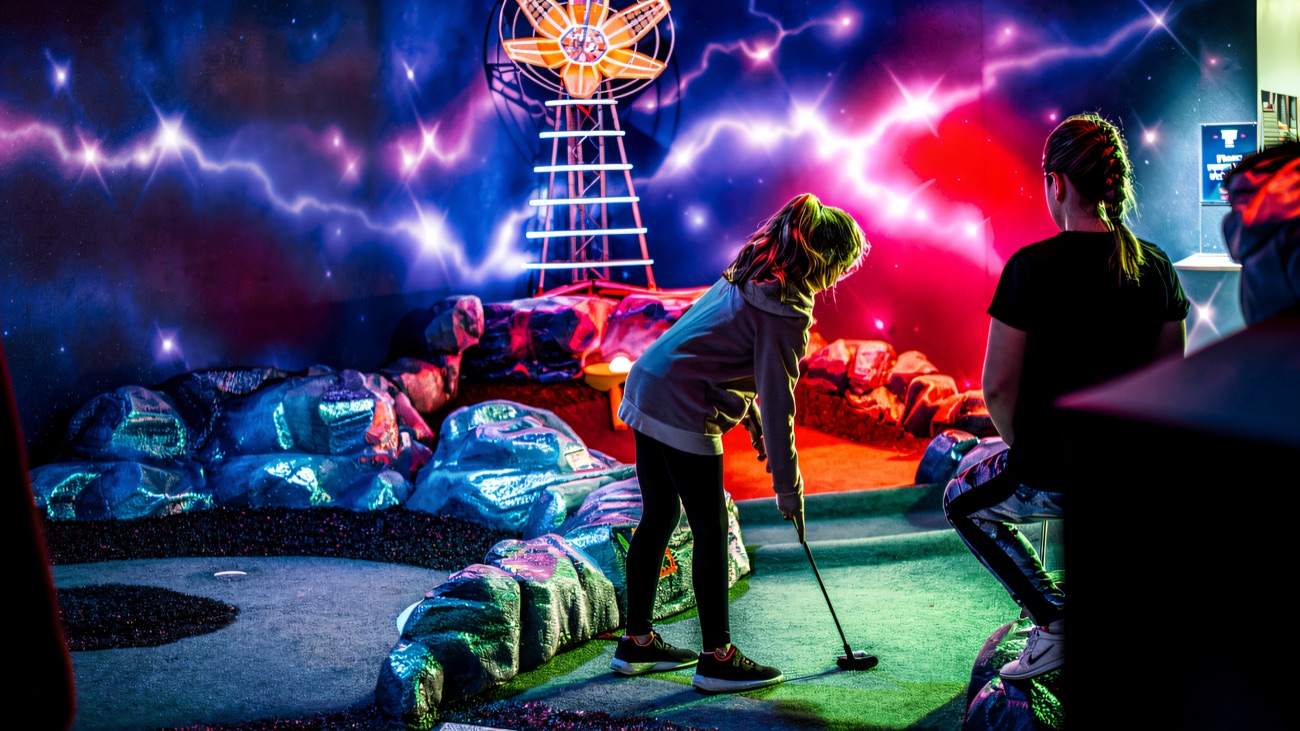 A young player lines up a putt beneath a glowing space tower on the neon nebula course