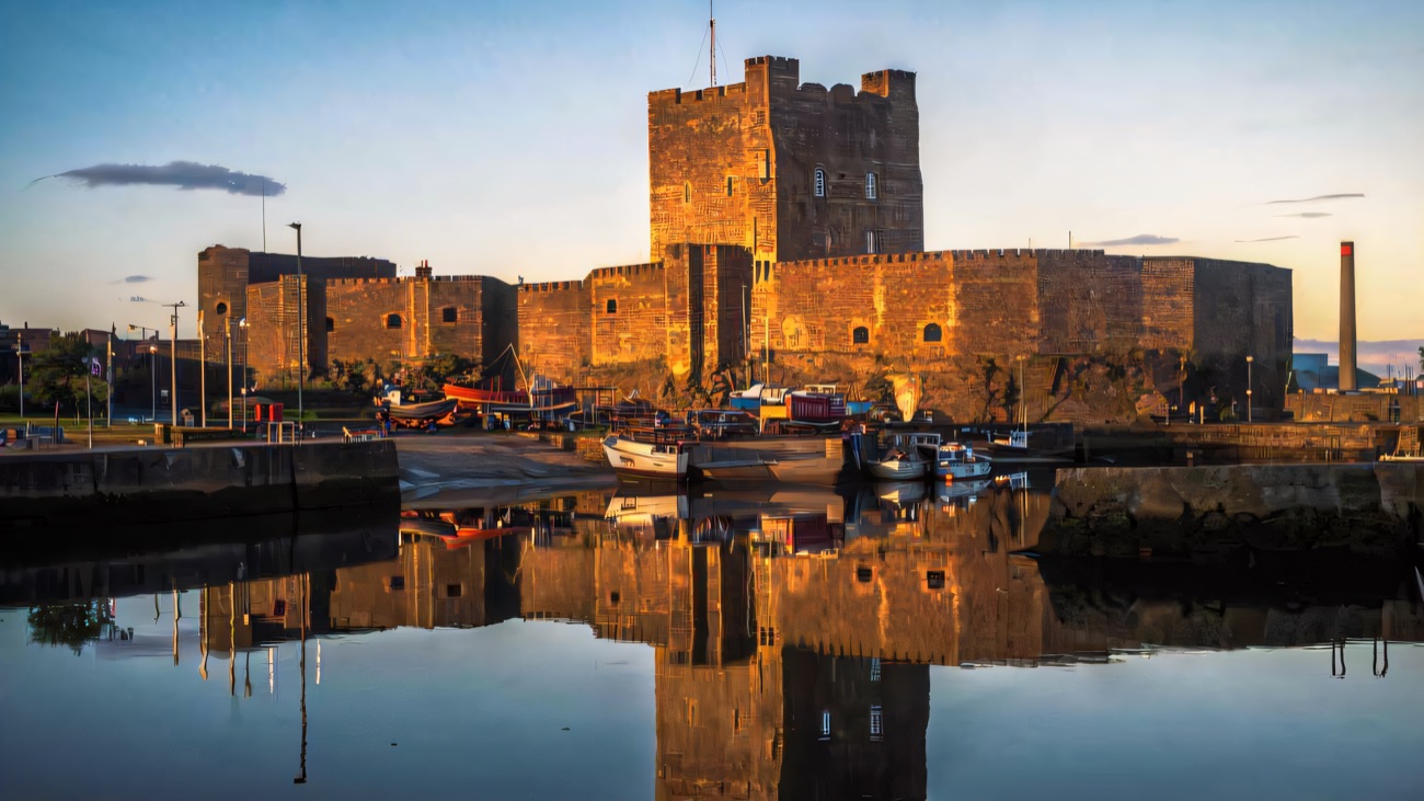 Carrickfergus Castle mirrored in the still harbour water at golden hour