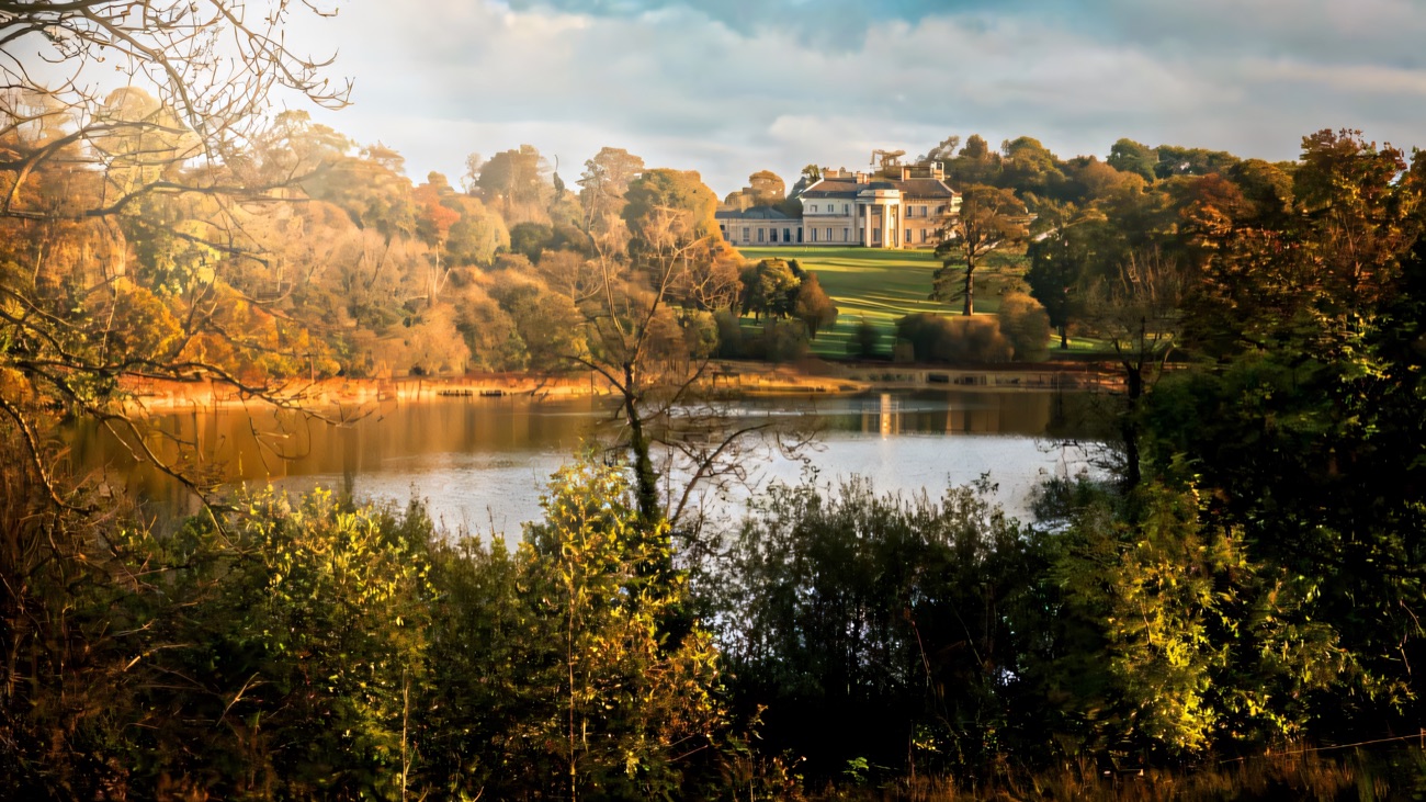 Castle Coole mansion on the rise above Lough Coole, seen across the water through autumn woods