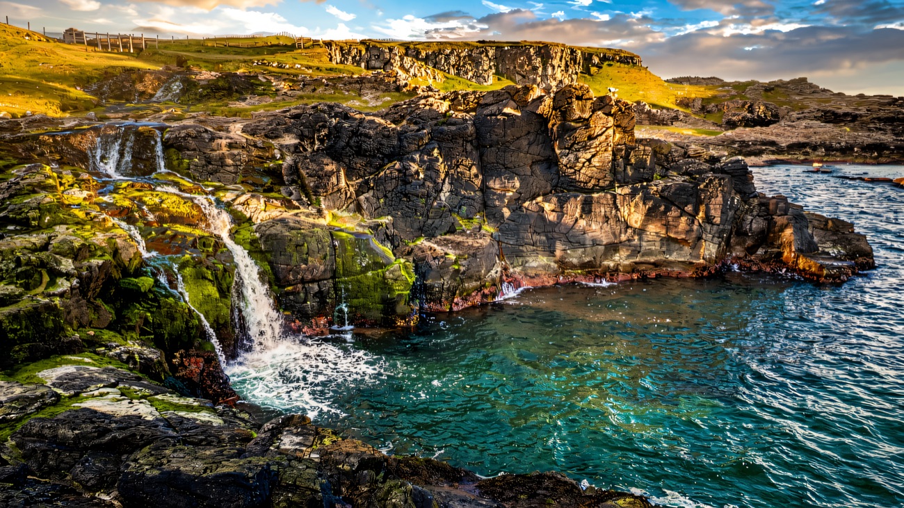 A little waterfall spilling down the black basalt into clear coastal water