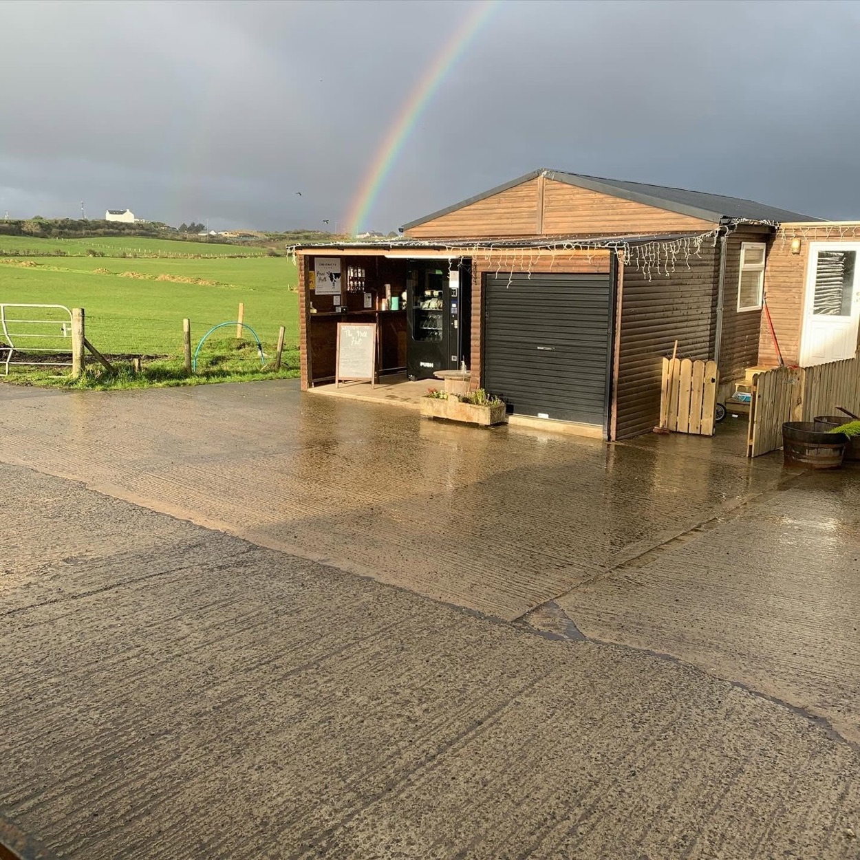The Milk Hut under a rainbow after a shower, with the green fields behind