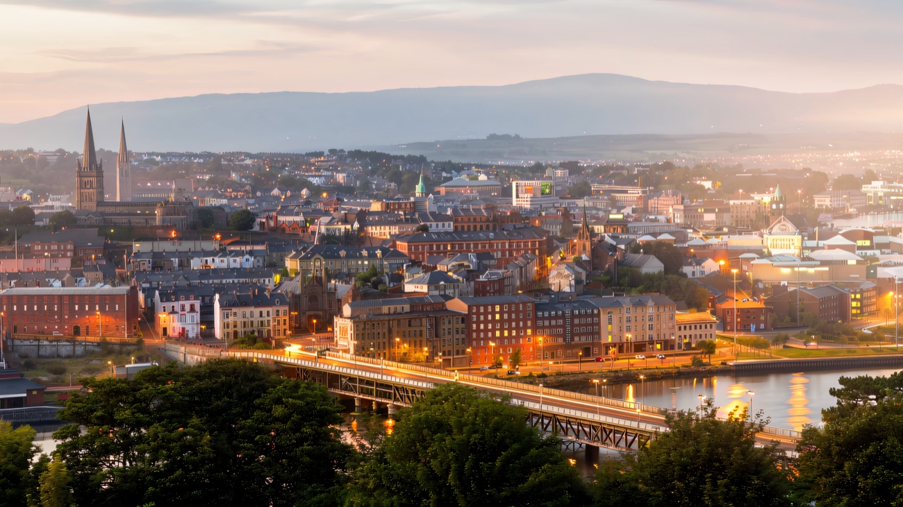 Derry's riverside skyline glowing at dusk, the Foyle winding through the city.