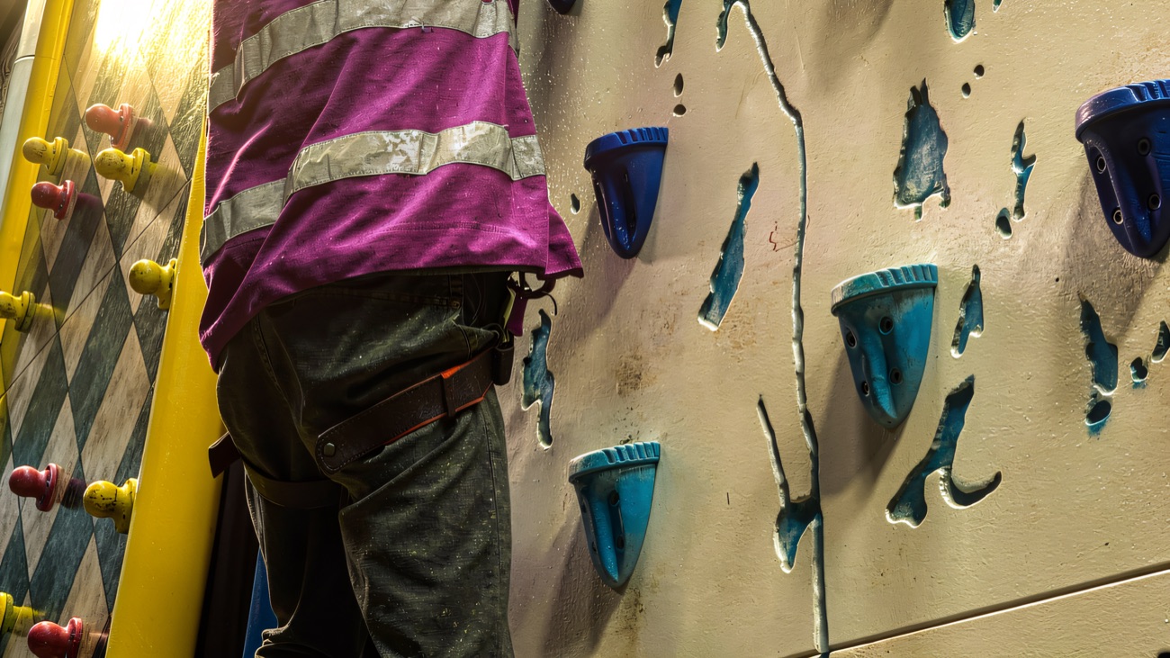 A climber working up a textured wall studded with blue and yellow holds