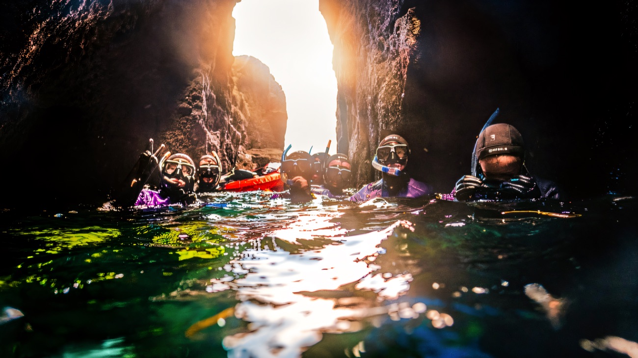 Snorkellers in masks bobbing at the surface inside a narrow rock gully
