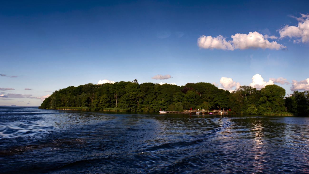 The whole tree-covered island seen from the lough on a clear blue day