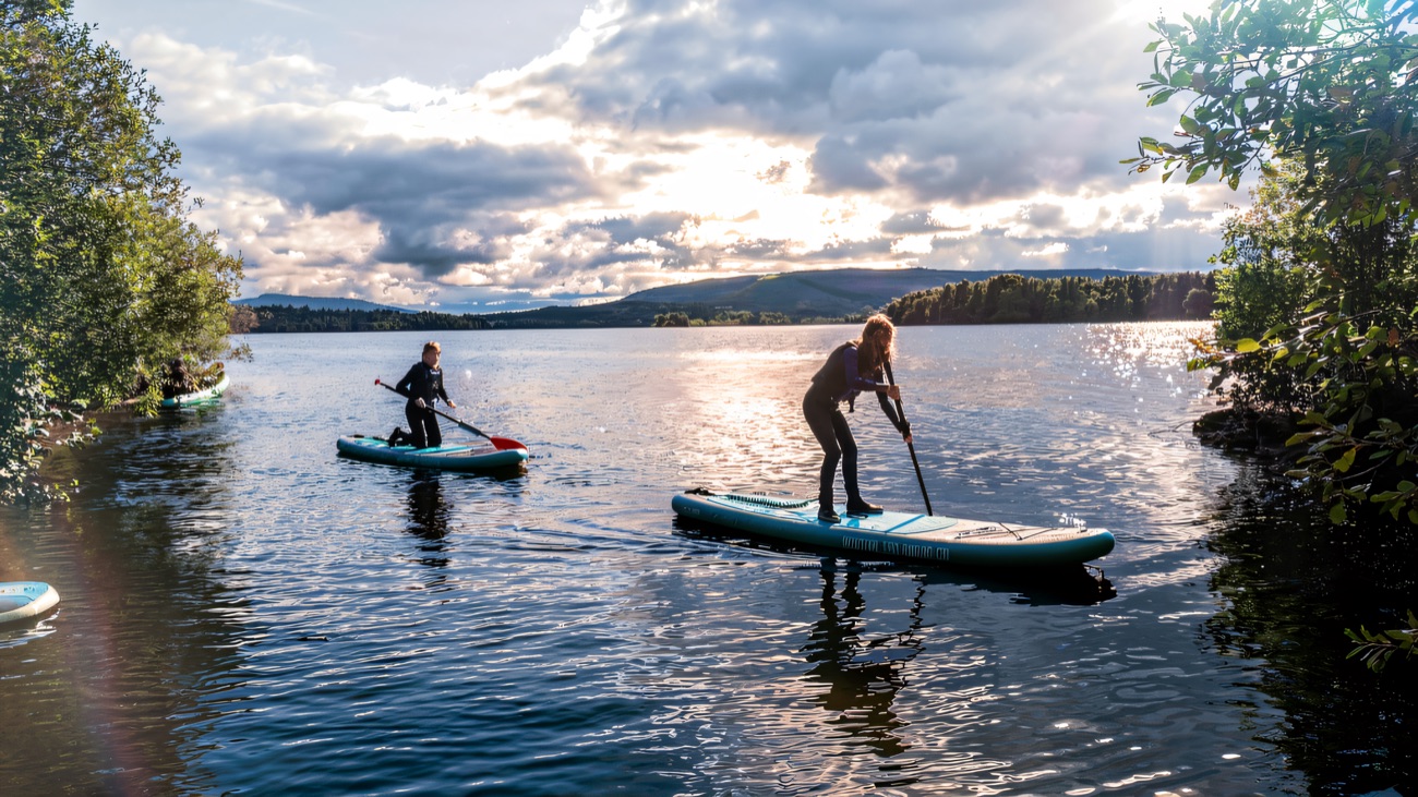 Paddleboarding across a mirror-calm lough with the hills beyond