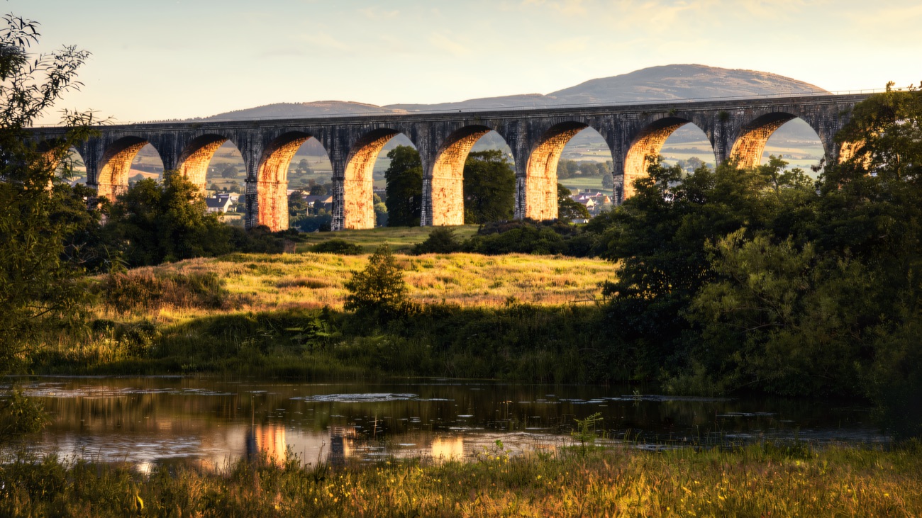 The great eighteen-arch viaduct at golden hour, reflected in the water in the valley below.