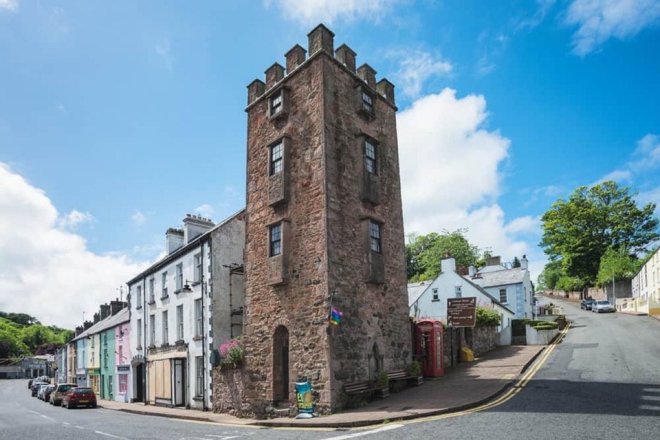 The red-sandstone Curfew Tower standing on a colourful village street corner in Cushendall, with a red phone box beside it under a blue sky