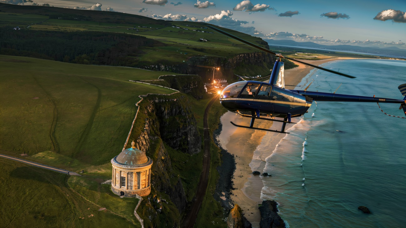 A blue helicopter in flight along the coast, with the domed clifftop temple and a long sandy beach below