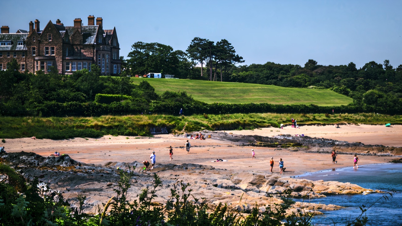 Families on the sand at Helen's Bay beach below the green lawns of Crawfordsburn Country Park