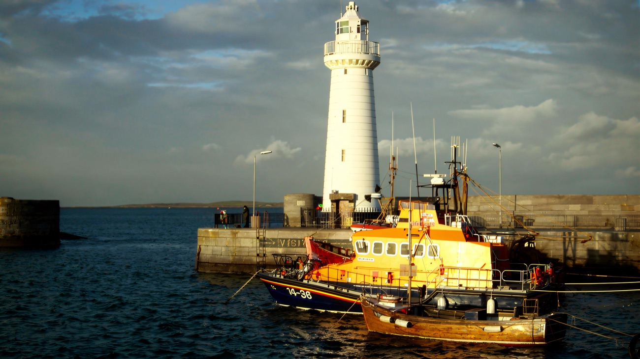 Warm evening light on the lighthouse and the orange RNLI lifeboat at its berth.