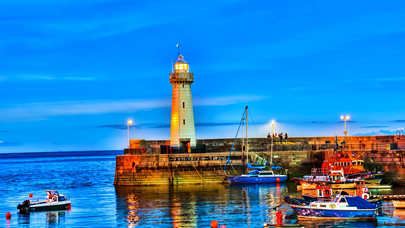 The white lighthouse at the end of Donaghadee's stone pier, with small boats and the lifeboat moored in the harbour