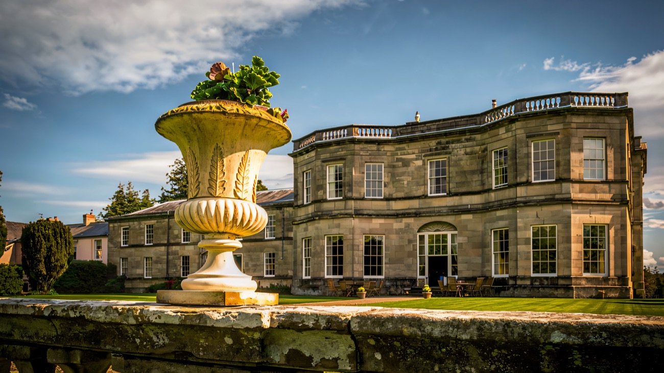 A carved stone urn on the terrace balustrade with the sunlit mansion behind