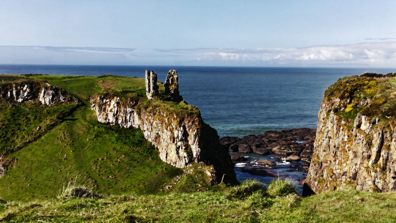 The lone ruin of Dunseverick perched on its headland, framed by grassy cliffs above the open sea.