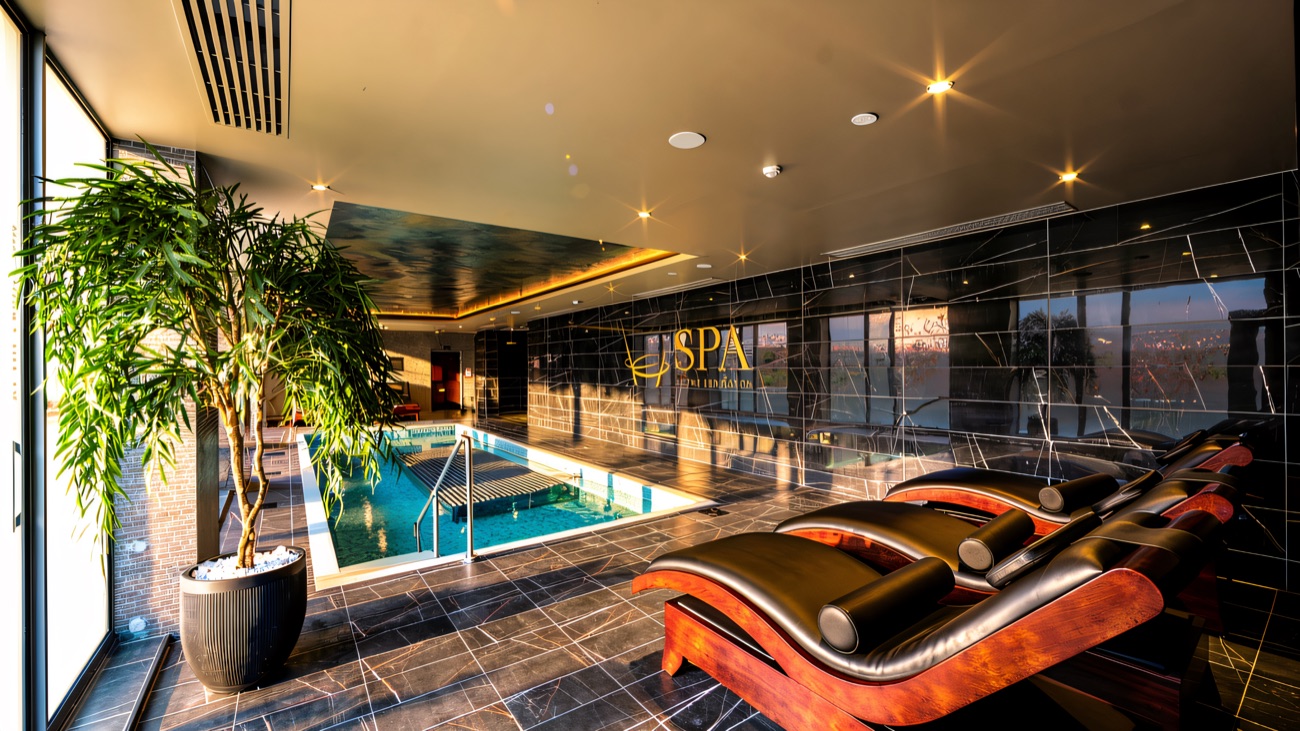 The spa's therapeutic pool with heated bubble loungers alongside, dark marble walls and a floor-to-ceiling window.