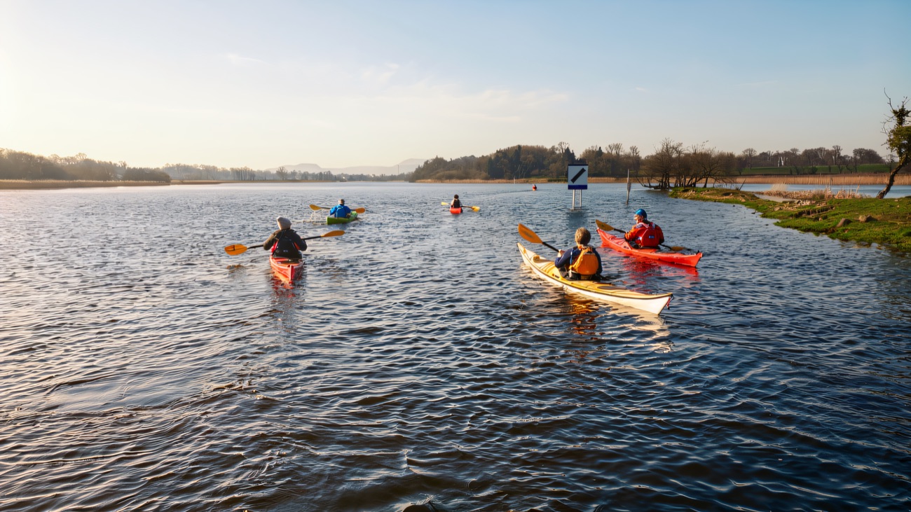A group of kayakers setting out together across calm Lough Erne.